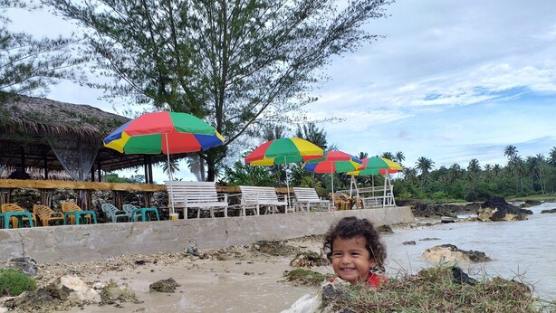 A beachside area with colorful umbrellas, lounge chairs, and a rocky shoreline.