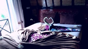 A bed with a heart-shaped towel, a brown blanket, and white flowers. - Bale Sasak (Gili Trawangan)