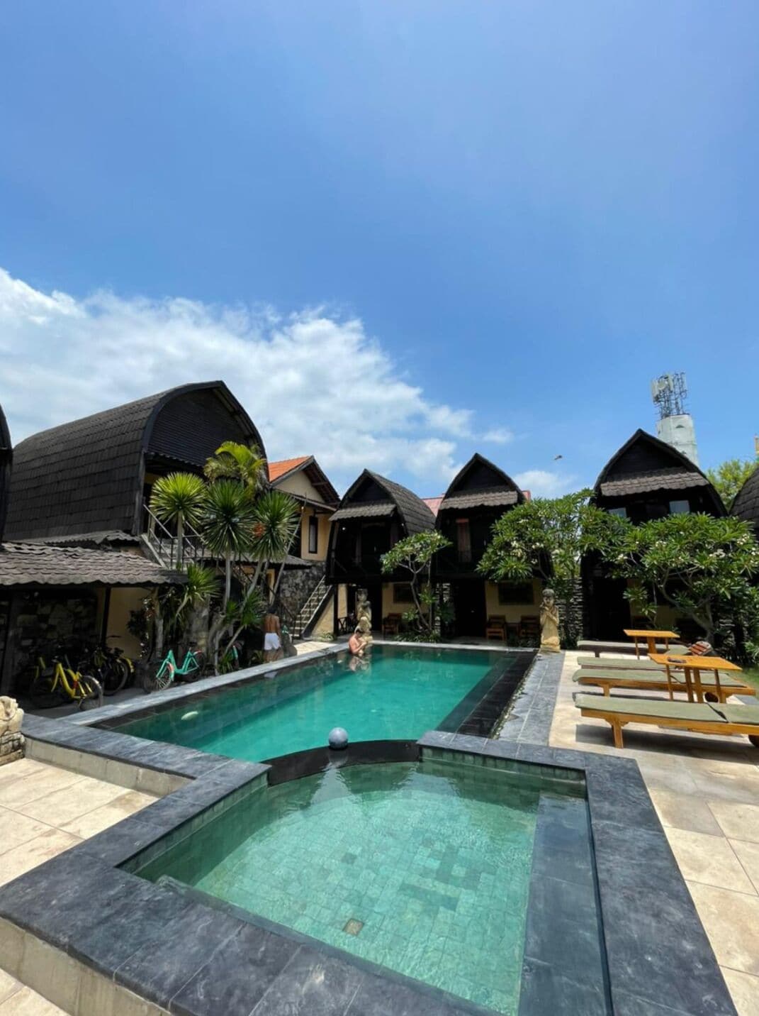 A pool area with overwater bungalows, a clear sky, and a statue.