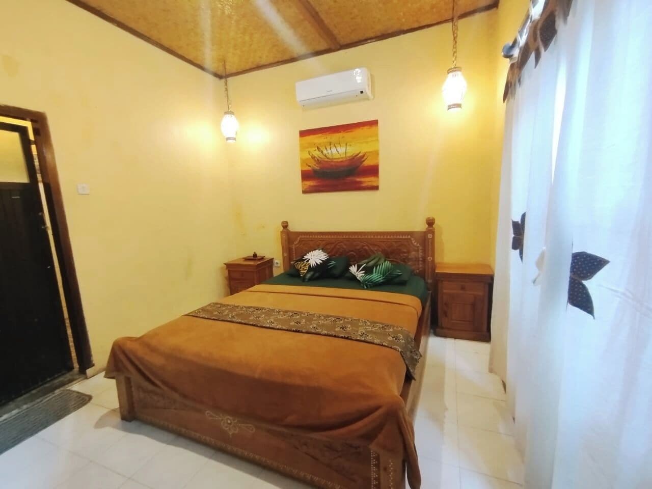 A bedroom with a bed, a nightstand, an air conditioner, and a painting on the wall.