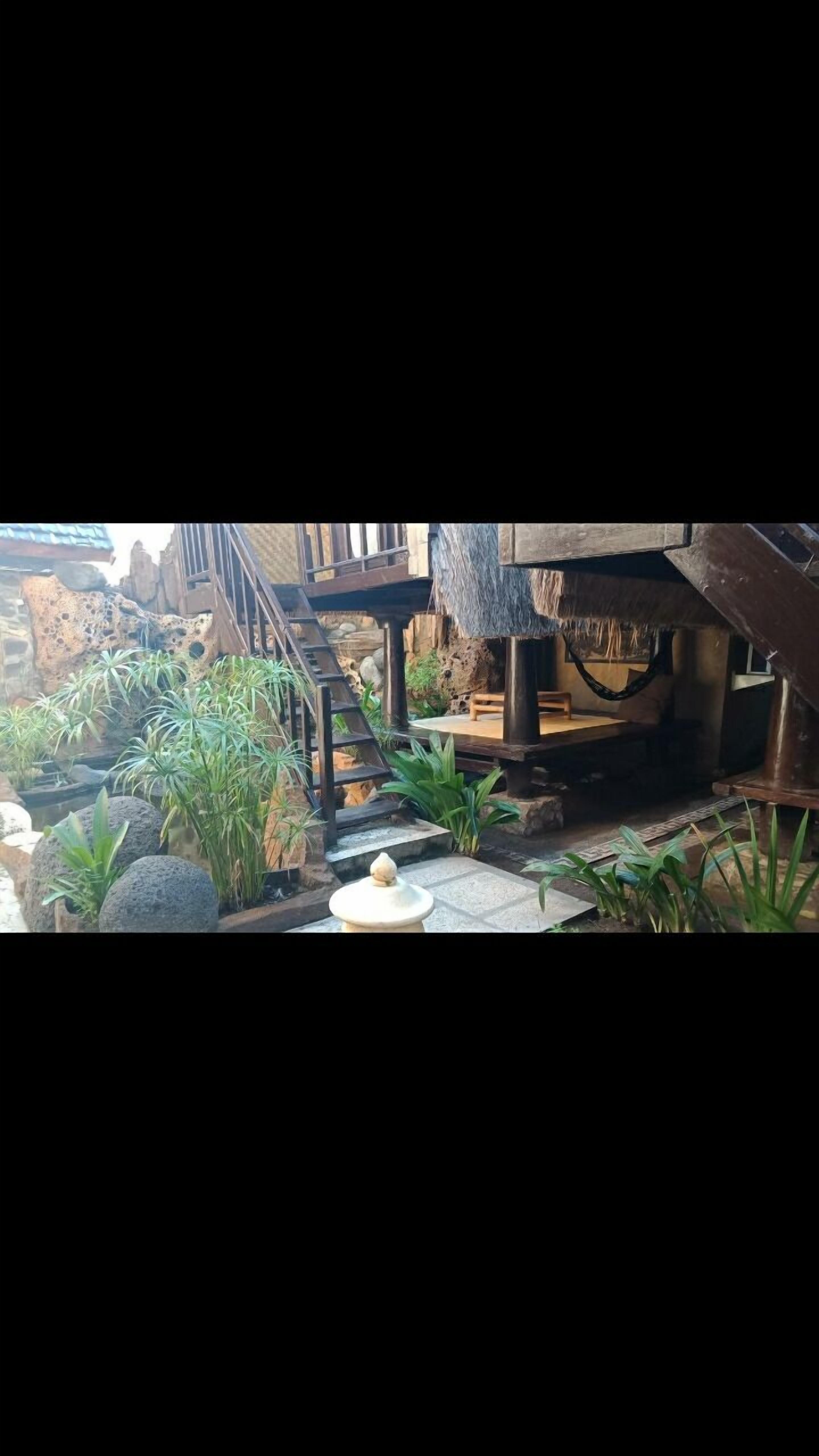 A rustic outdoor area with a stone staircase, wooden deck, and a thatched roof structure.