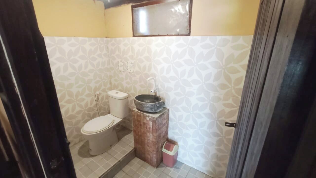 A small bathroom with a toilet, a sink with a basin, and a trash bin.