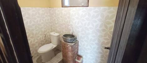 A small bathroom with a toilet, a sink with a basin, and a trash bin.