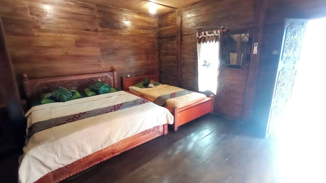 Una habitación de madera con dos camas, techo de madera y una ventana con cortinas.
