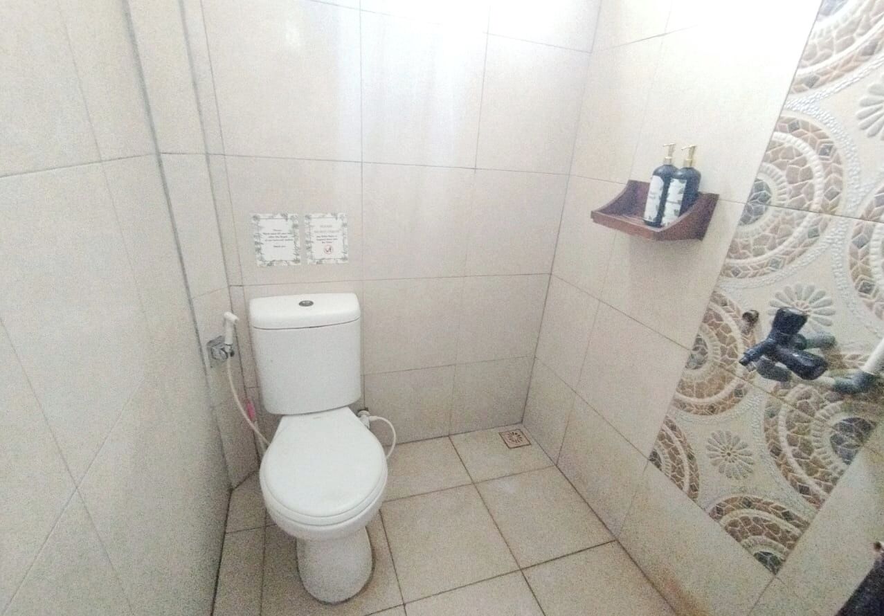 Et lille badeværelse med fliser, toilet, bruseafsnit og et hylder med toiletartikler.