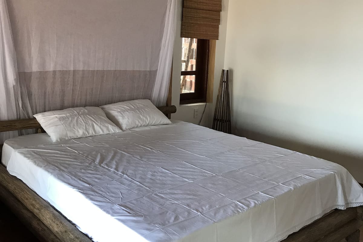 A bed with a wooden frame, white bedding, and a mosquito net.