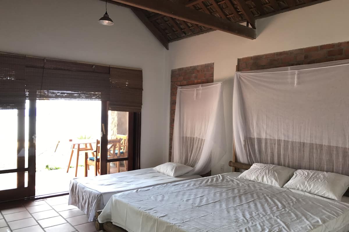 A room with two beds, a wooden ceiling, and a view of the outside.
