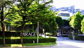 A hotel entrance with a sign reading "MIRAGE by the lake," surrounded by lush greenery and modern buildings in the background. - Pinebox Mirage by the Lake (Cyberjaya)