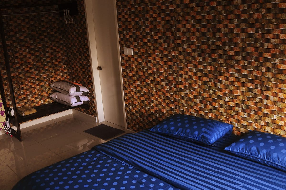 A bedroom with a patterned brick wall, a bed with blue bedding, and a door to the left.