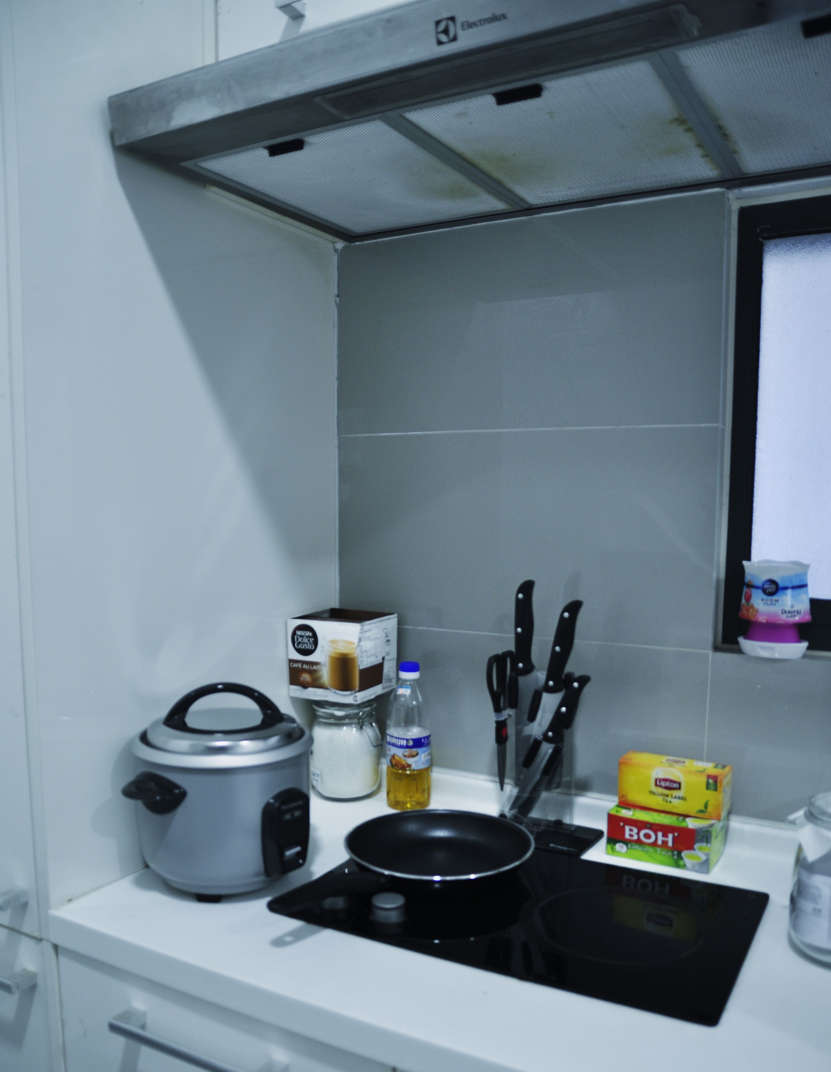 A kitchen with a stove, a pot, a bottle of oil, a box of Lipton tea, a box of Bohlmann coffee, and a set of knives on the counter.