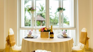 A round table with a white tablecloth, two chairs with gold sashes, a bottle of champagne, a floral centerpiece, and two hanging flower baskets. - Navy Hotel Danang (Da Nang)