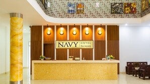 A reception desk with a sign reading "NAVY HOTEL DANANG" and a wooden panel backdrop. - Navy Hotel Danang (Da Nang)