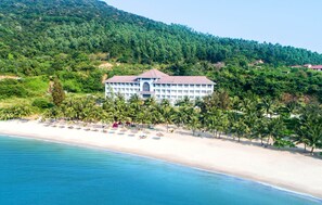 A beachfront hotel with a large building, palm trees, and a sandy beach. - Navy Hotel Danang (Da Nang)