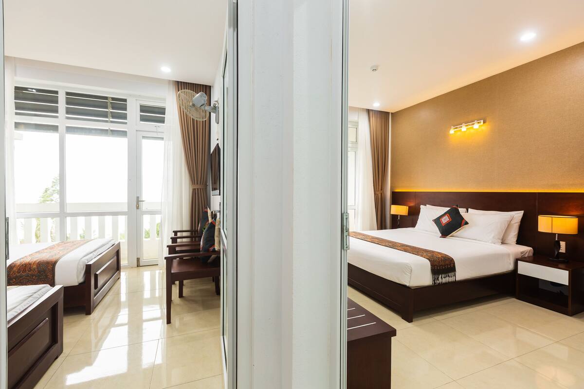 A hotel room with a large bed, a desk, a chair, and a balcony with curtains.