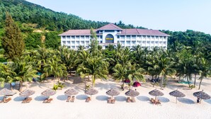 A hotel with a central building surrounded by palm trees and beach umbrellas. - Navy Hotel Danang (Da Nang)