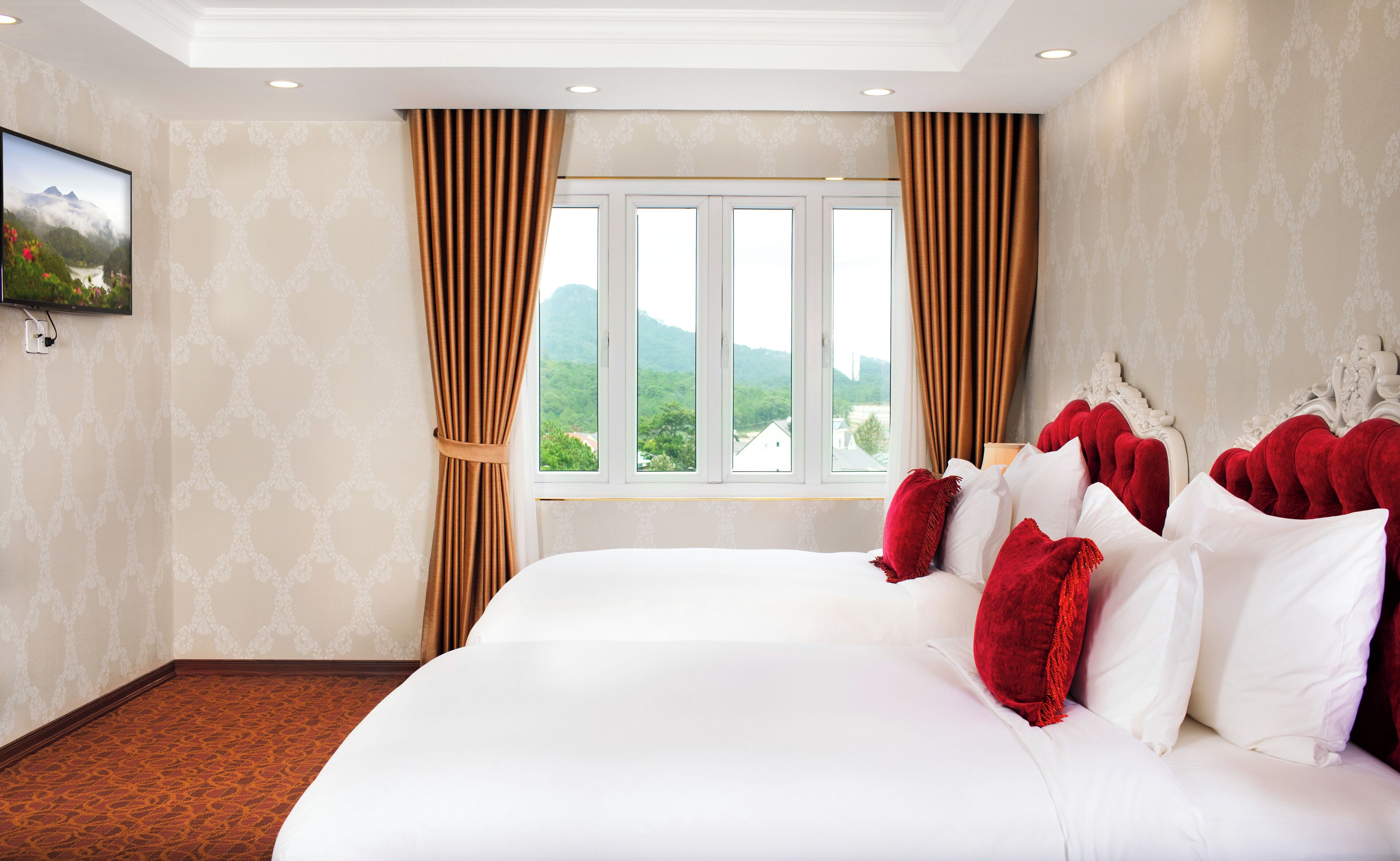 Ein Hotelzimmer mit einem großen Bett, roten Kissen und Blick auf Berge durch das Fenster.
