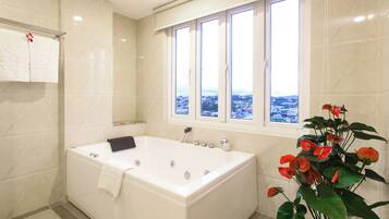A modern bathroom with a large bathtub, a window with a city view, and a potted plant with red flowers.