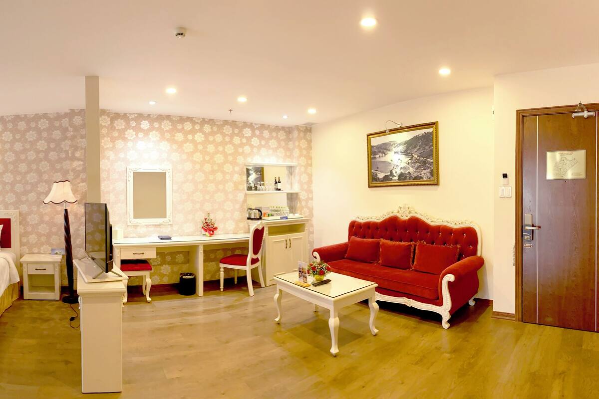Habitación de hotel con dos camas, un escritorio, un sofá rojo, un espejo y una puerta.