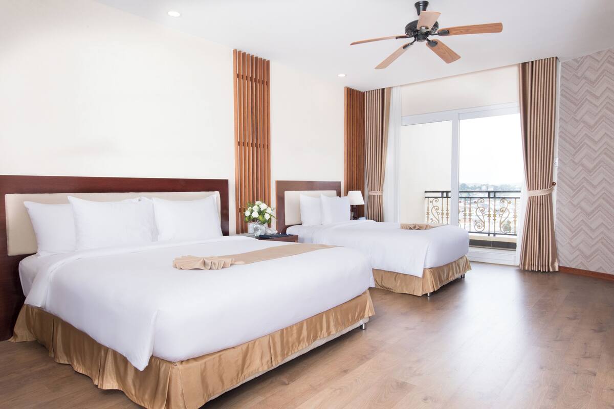 Habitación de hotel con dos camas, ventilador de techo y balcón con barandilla.