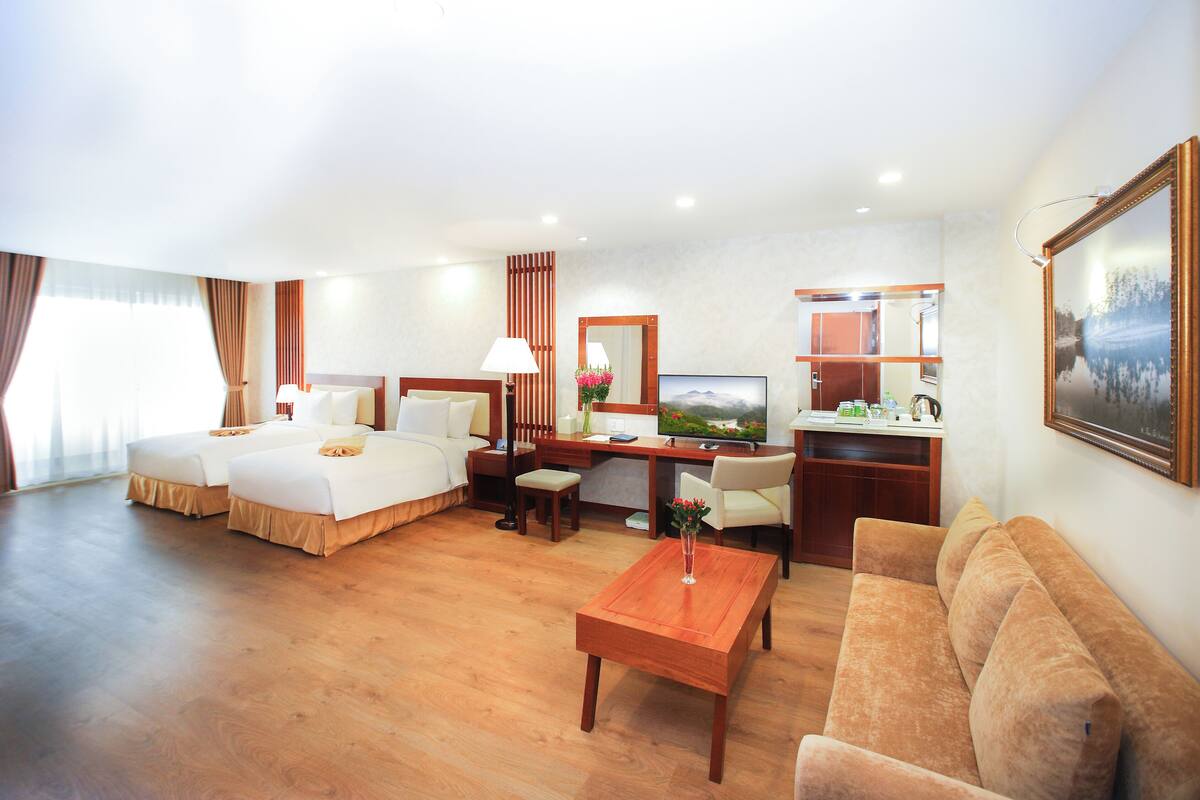 Habitación de hotel con dos camas, un escritorio, un sofá, una mesa de centro y un televisor.
