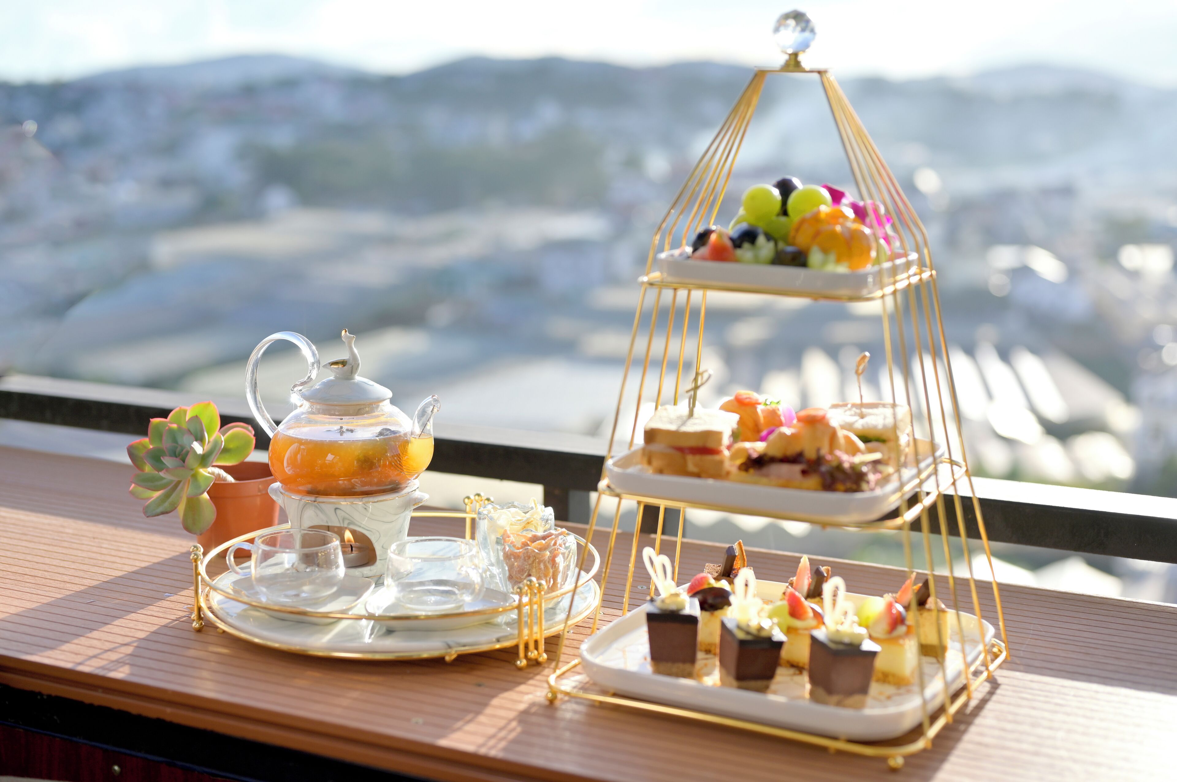A tiered dessert display with various pastries and a teapot on a wooden table.