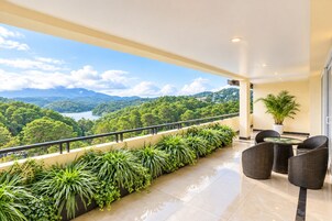 Un balcón con vista a un lago y montañas, amoblado con sillas de mimbre y una mesa.