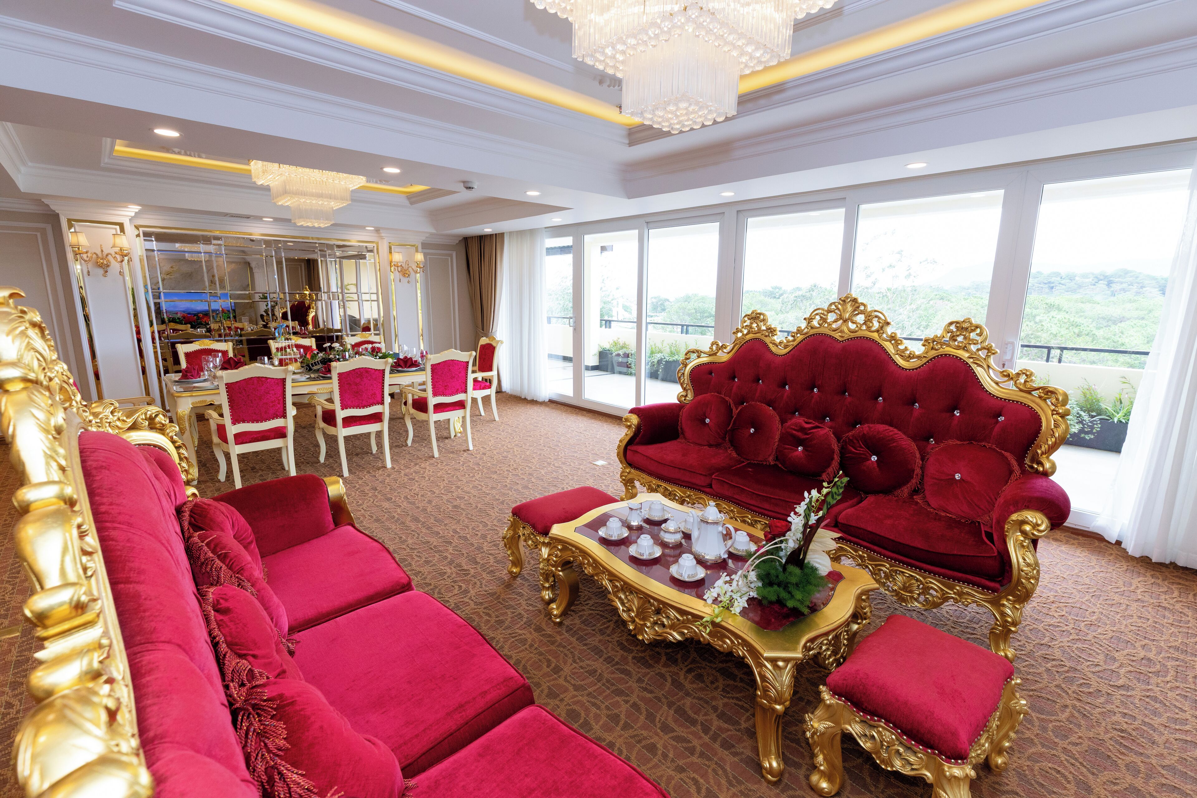 A luxurious room with a red sofa, gold-framed armchairs, and a dining area with white chairs.