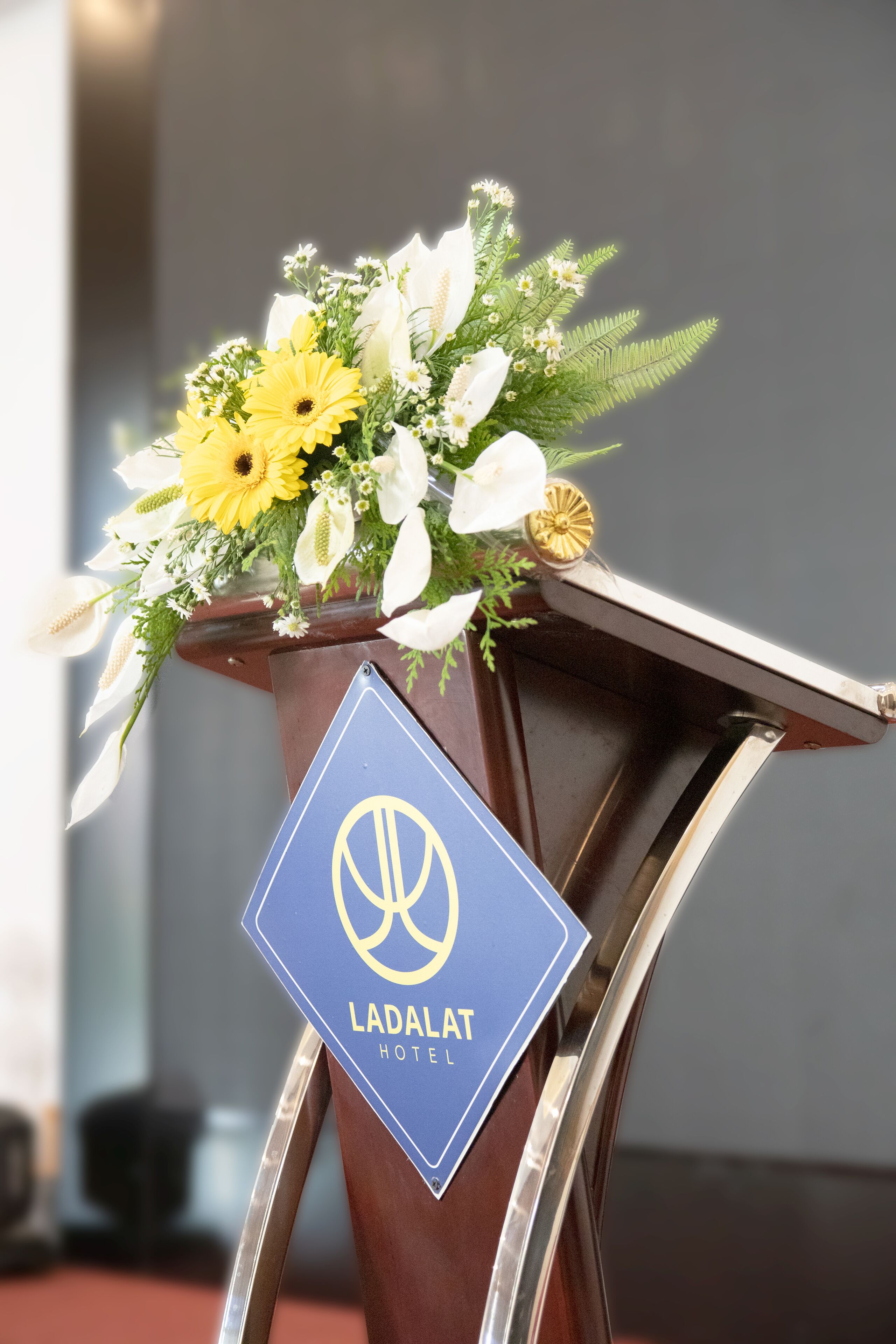 A podium with a blue sign reading "LADALAT HOTEL" and a floral arrangement on top.