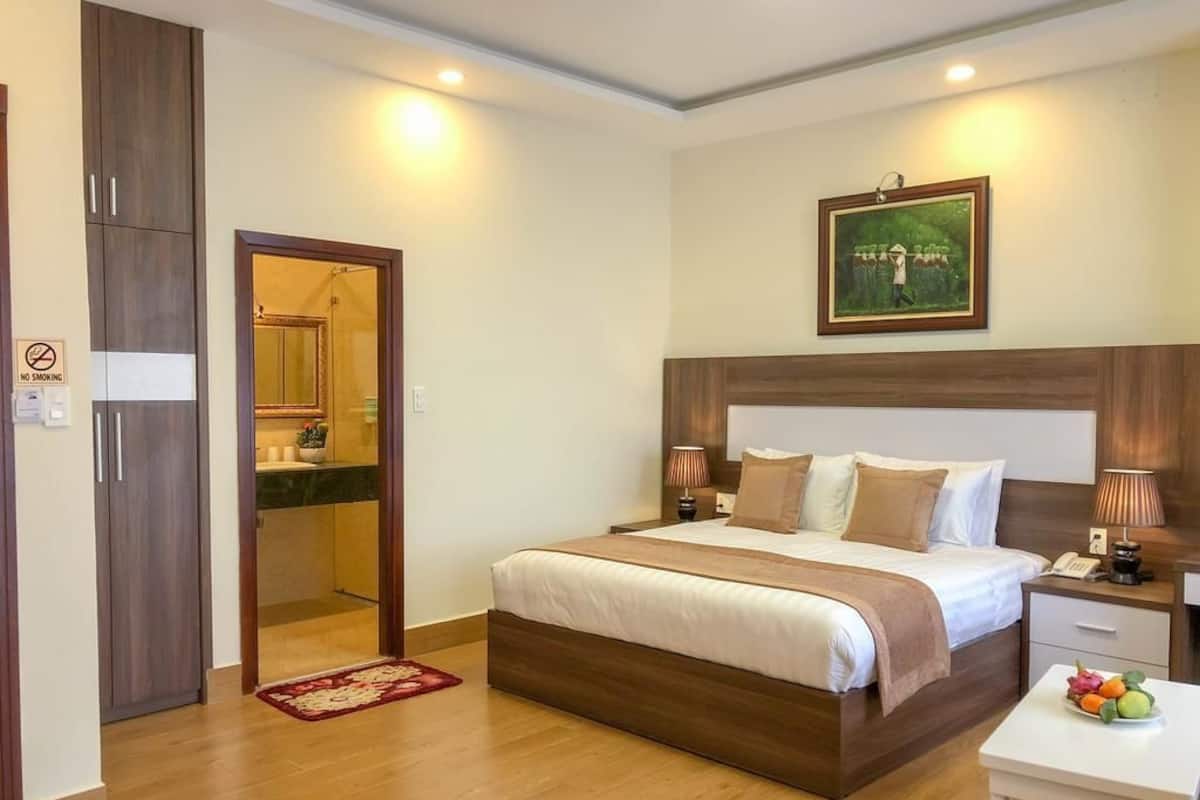 A bedroom with a bed, bedside tables, a nightstand, a mirror, a door, and a small table with fruit.