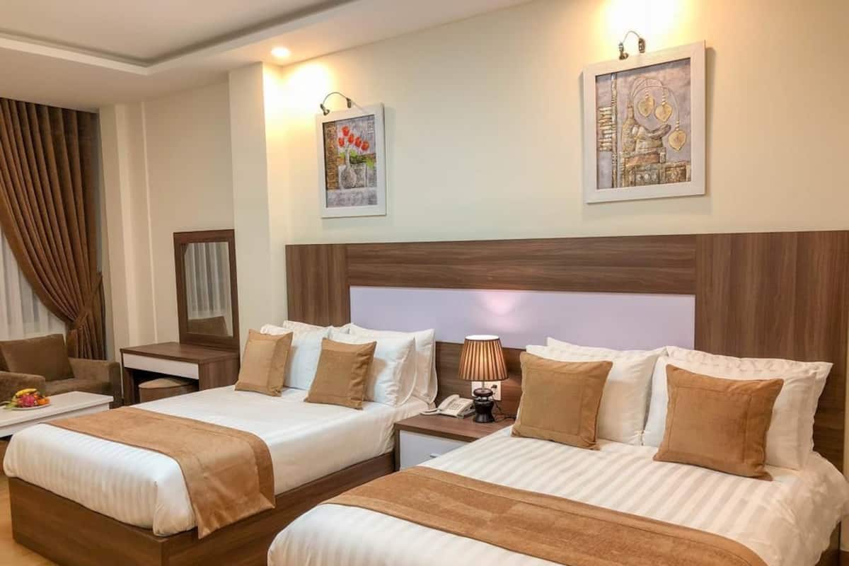 A hotel room with two beds, a desk, a chair, and artwork on the walls.