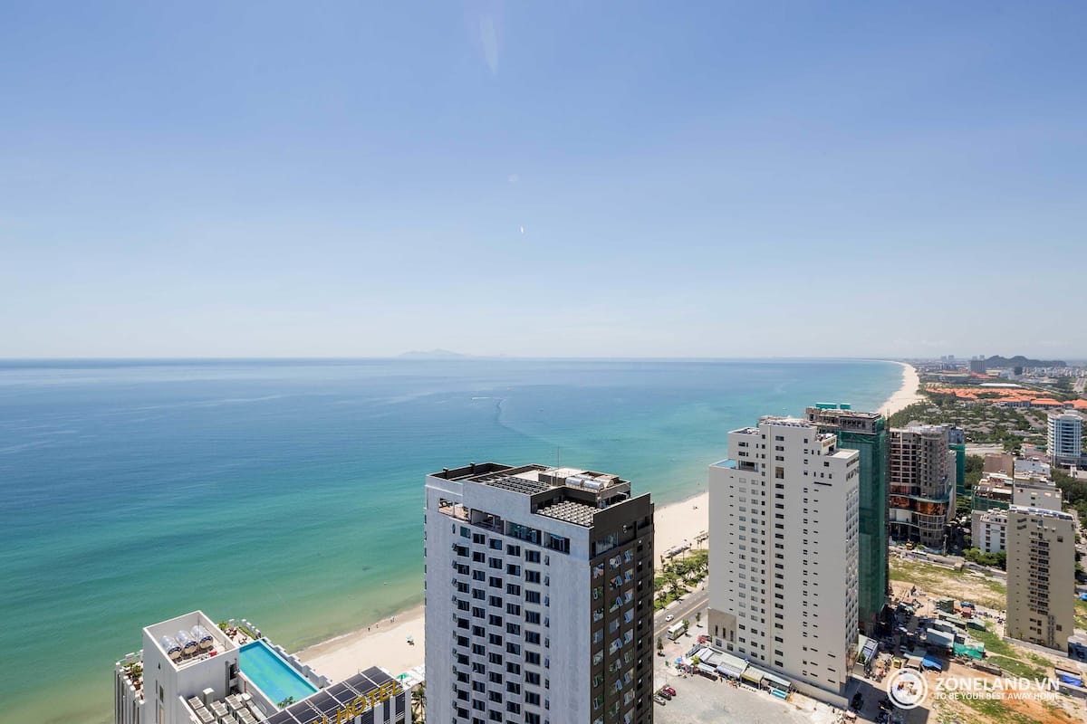 Een hoog hotel met een zwembad op het dak, met uitzicht op een strand en de oceaan.