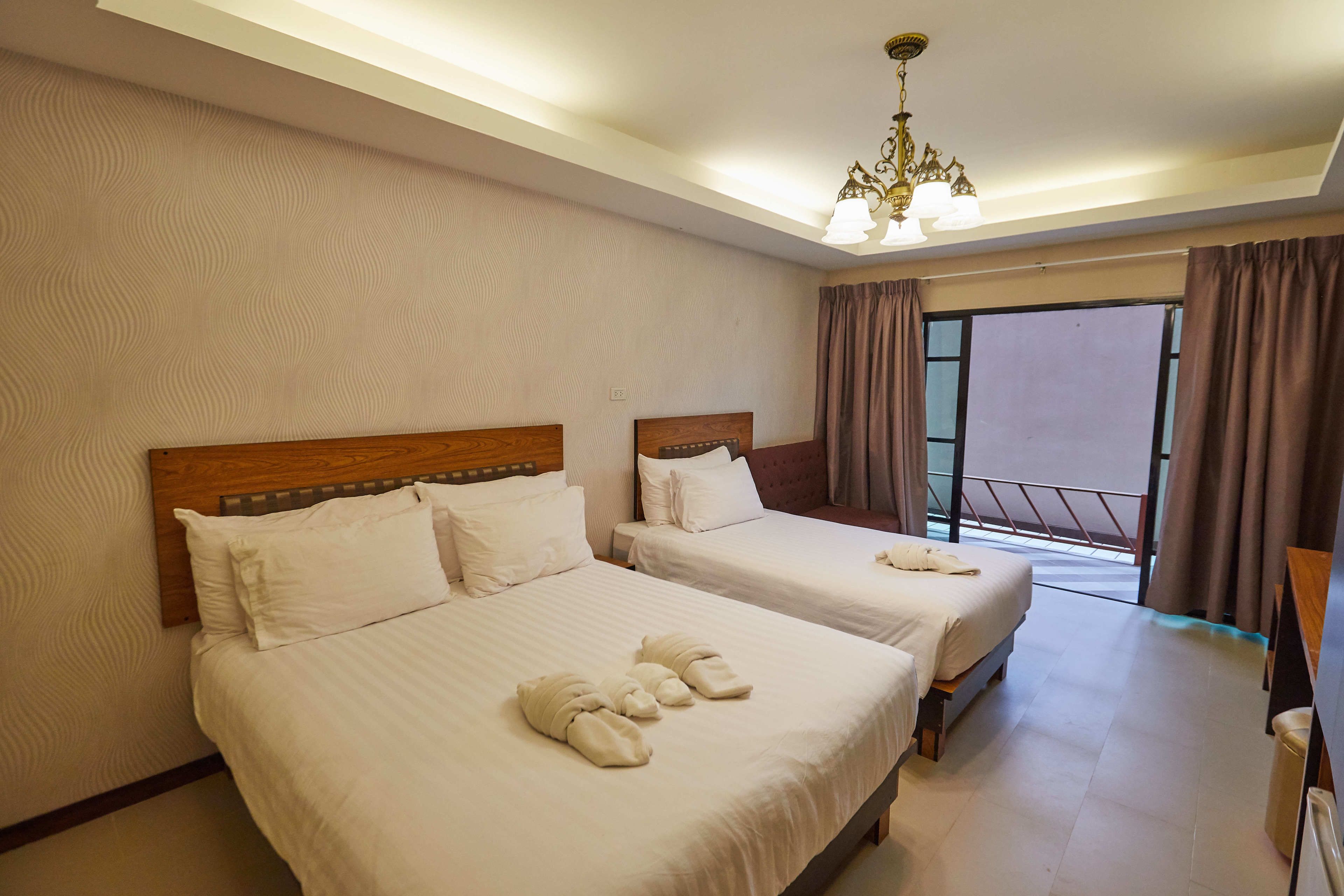 Quarto de hotel com duas camas, um lustre e vista para o exterior.