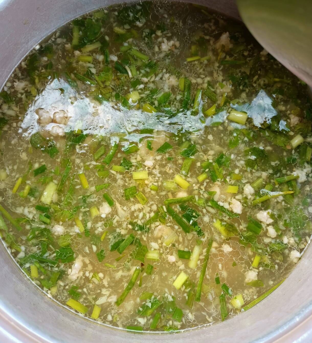 A pot of soup with green vegetables and possibly tofu or mushrooms.