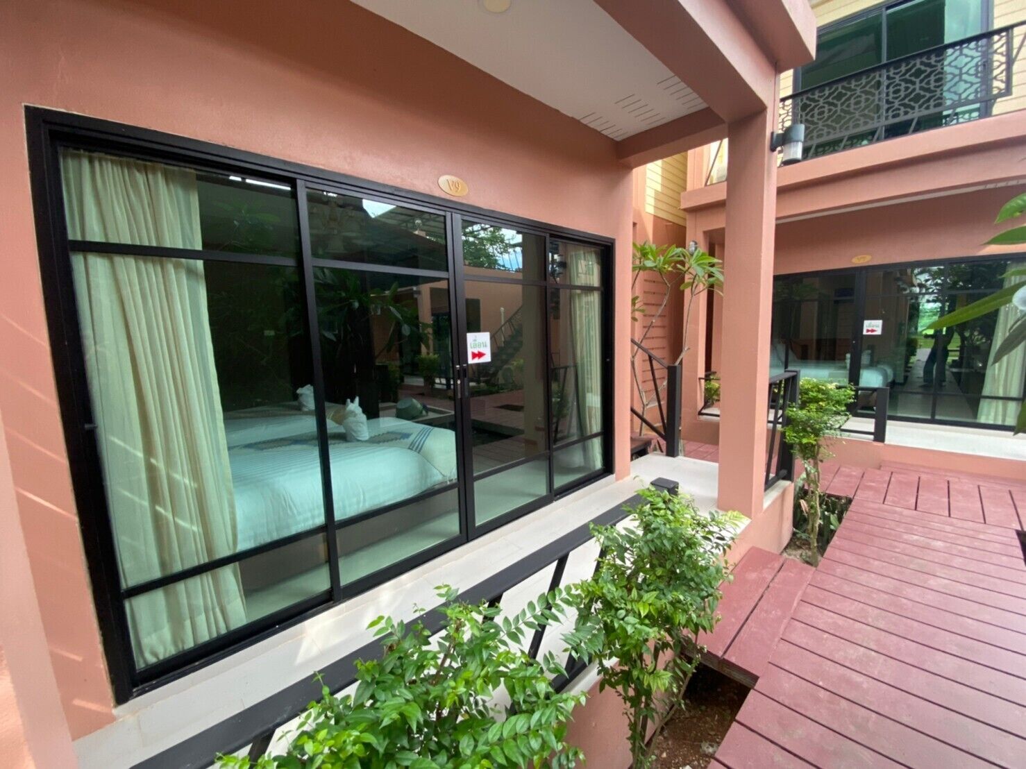 A hotel room with large sliding glass doors, a bed, and a small balcony with potted plants.