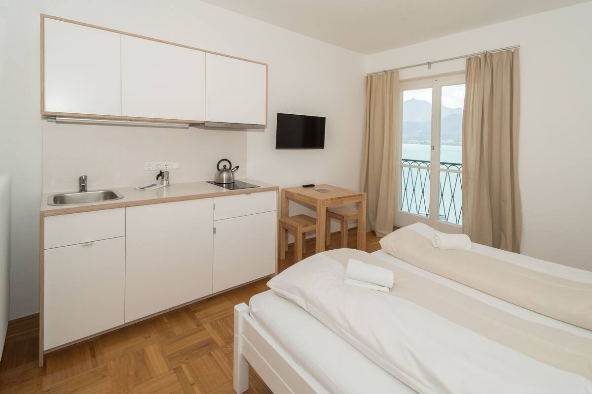 Ein Hotelzimmer mit Küchenzeile, einem Bett, einem Fernseher und einem Balkon mit Aussicht.