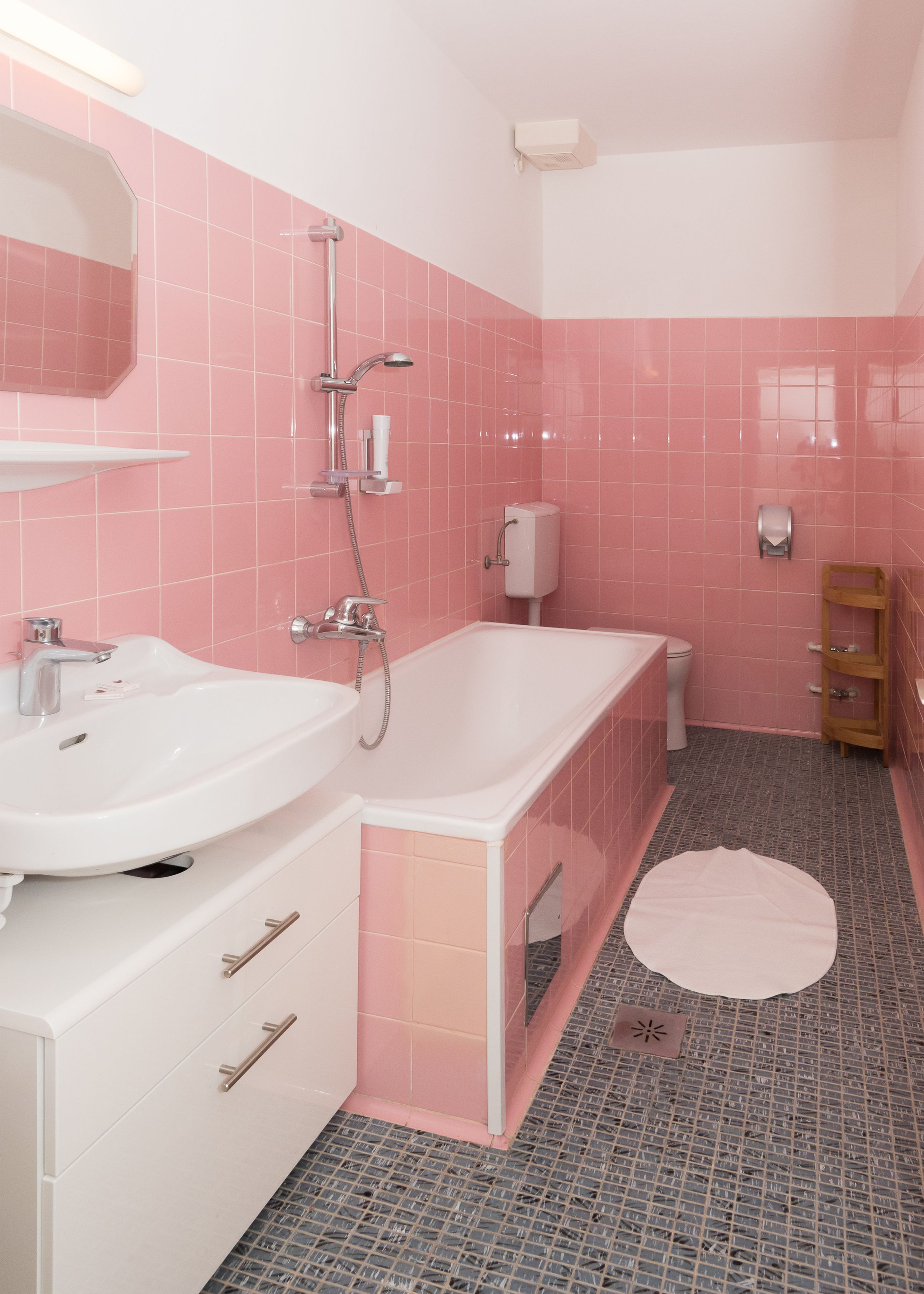 A bathroom with pink tiles, a white sink, a bathtub, and a wooden shelf.