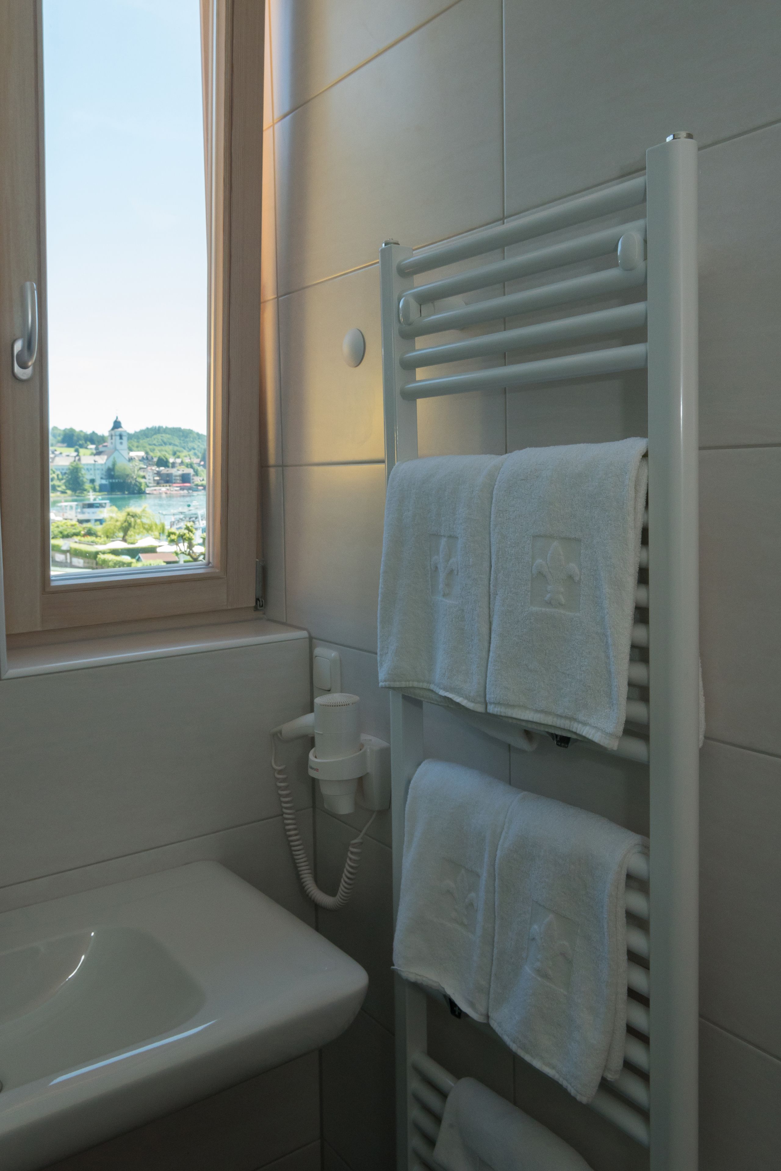 Un baño con ventana, lavamanos y toallero con toallas.