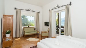 A bedroom with a large bed, a wooden wardrobe, a small table with a plant, two chairs, and a view of the outdoors through a window. - Seehaus Familie Leifer (Sankt Wolfgang im Salzkammergut)