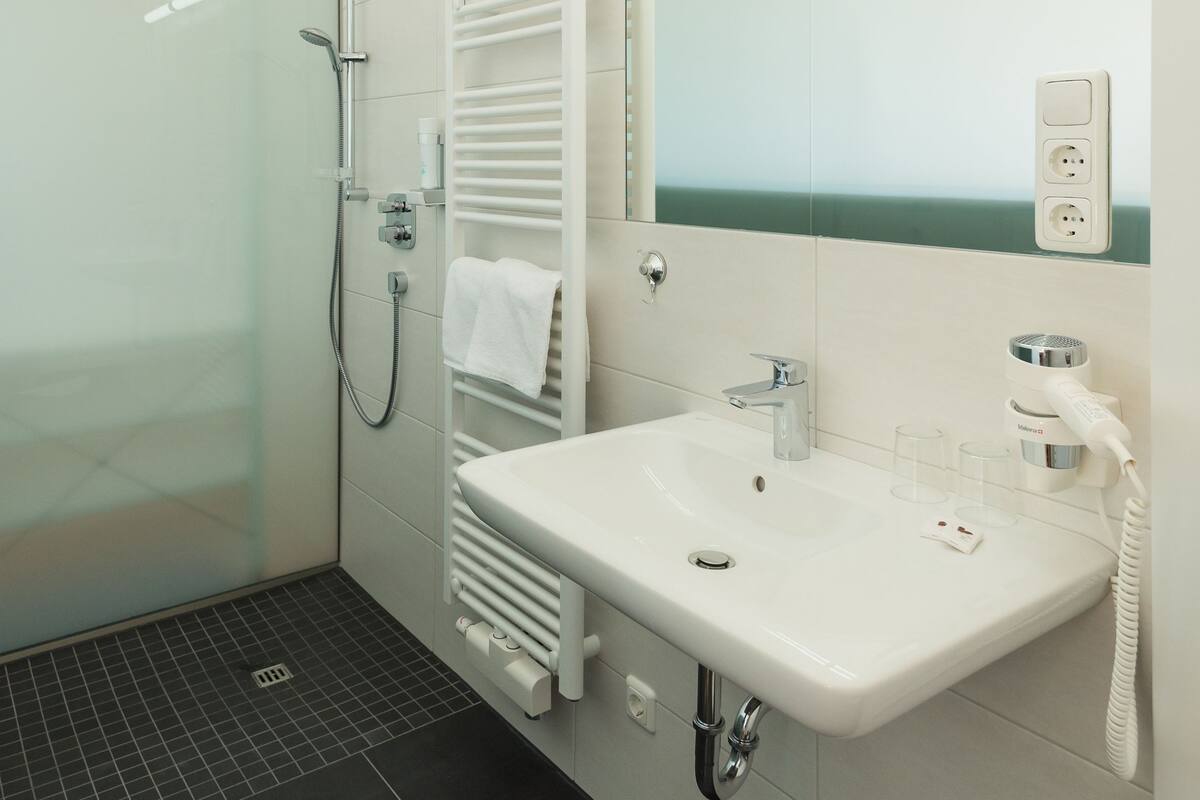 Ein modernes Badezimmer mit einer in Glas eingefassten Dusche, einem weißen Waschbecken und einem großen Spiegel.