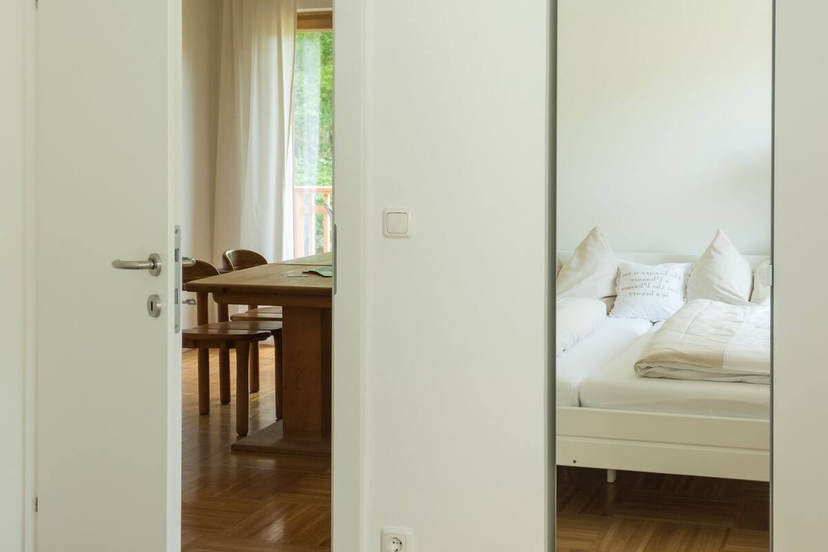 Ein Schlafzimmer mit Bett, Holzboden, Essbereich mit Tisch und Stühlen sowie einem großen Spiegel.