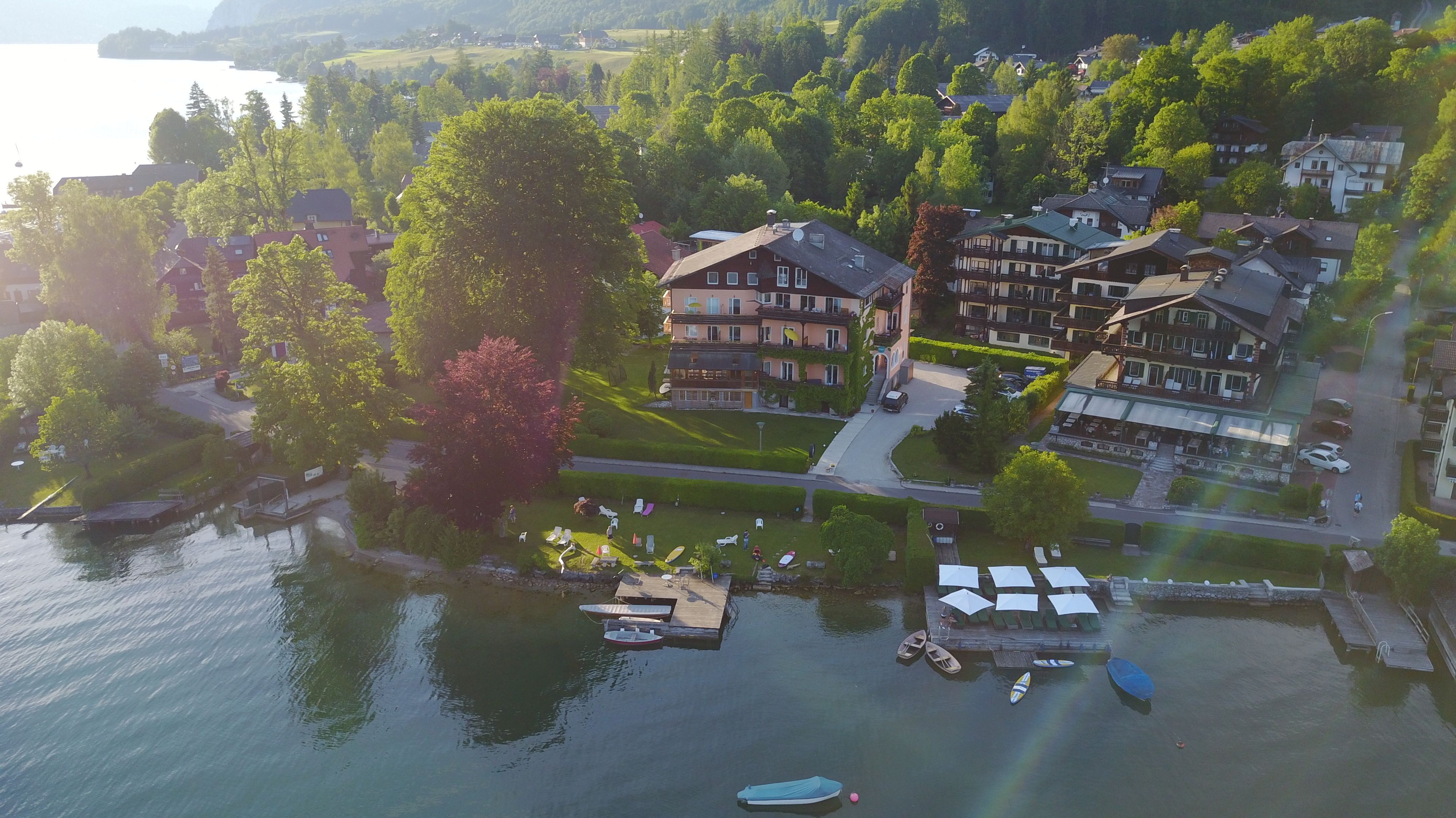 An aerial view of a lakeside property with multiple buildings, a dock with boats, and a well-maintained lawn.