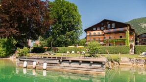 A lakeside hotel with a dock, outdoor seating, and a mountain backdrop. - Seehaus Familie Leifer (Sankt Wolfgang im Salzkammergut)