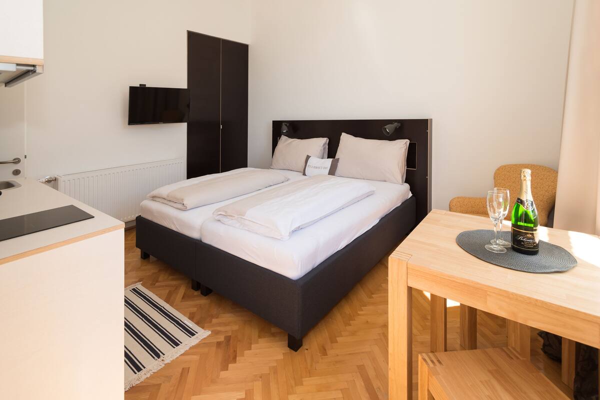 Ein ordentlich eingerichtetes Schlafzimmer mit Bett, Nachttisch und einem kleinen Tisch mit Flasche und Glas.