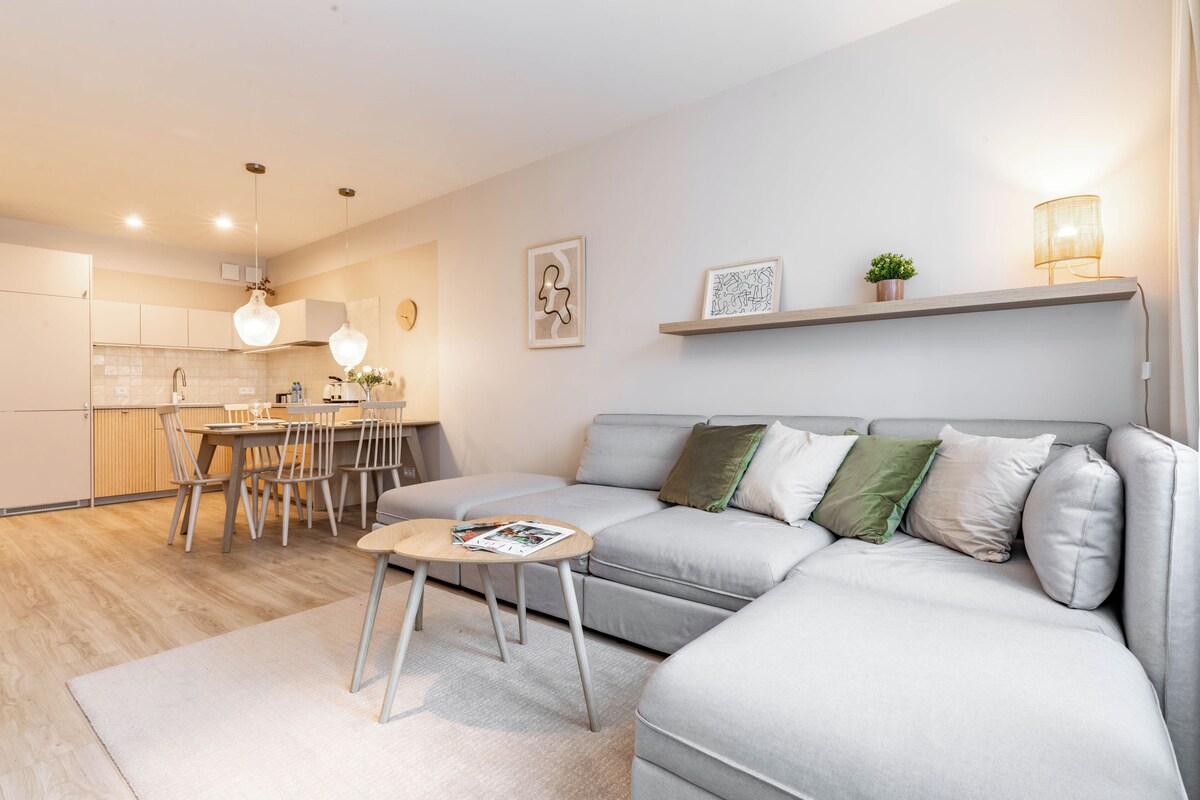 A modern living room with a grey sofa, a coffee table, and a dining area with chairs and a table.