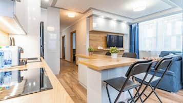 A modern kitchen with a built-in island, a dining area with a blue sofa, and a living room with a TV.