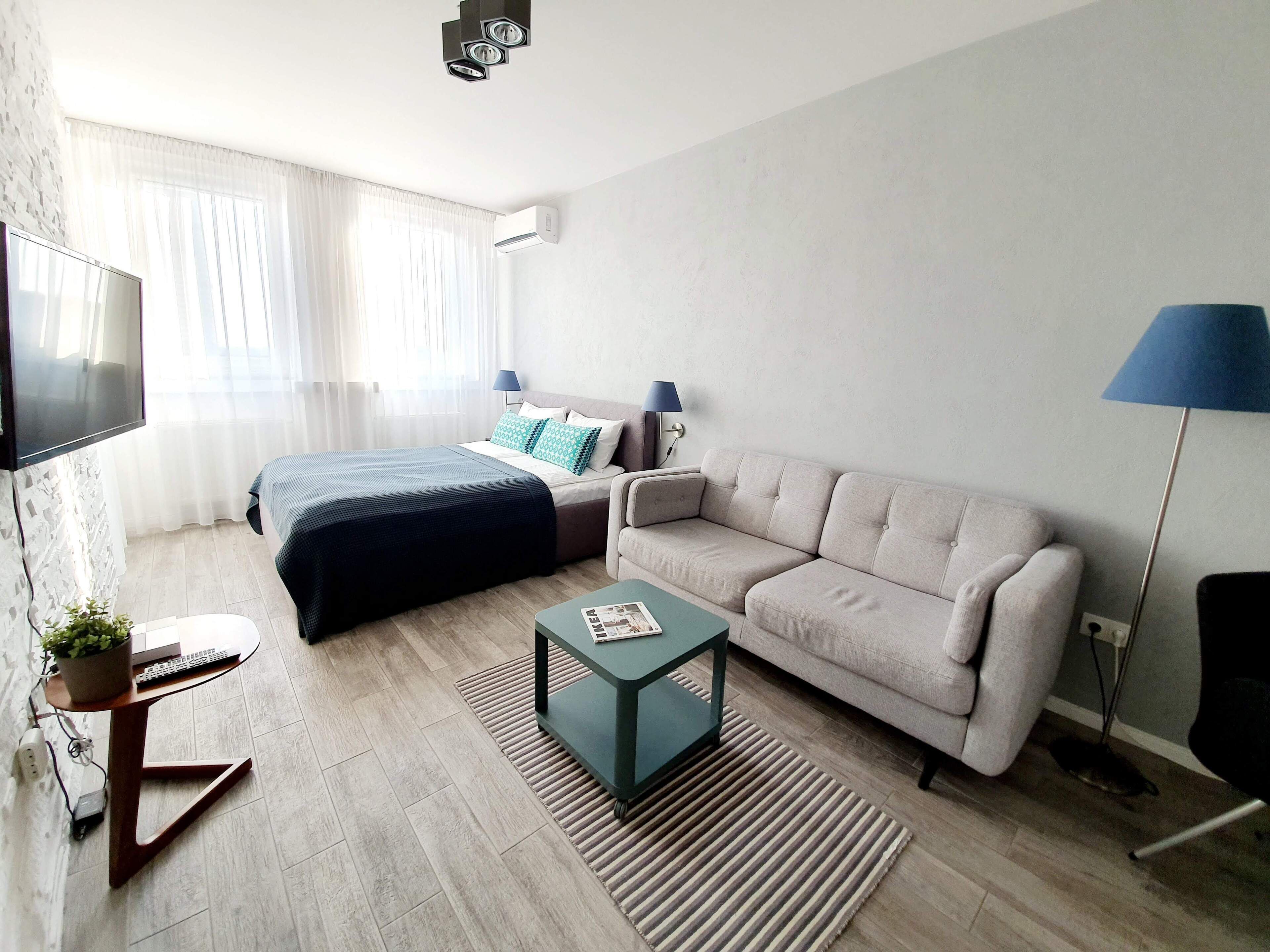 Una habitación de hotel moderna con cama, sofá, televisor, escritorio y una pequeña mesa con una planta.