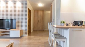 Una cocina moderna con microondas integrado, un pequeño comedor con banco, y un televisor en la sala.