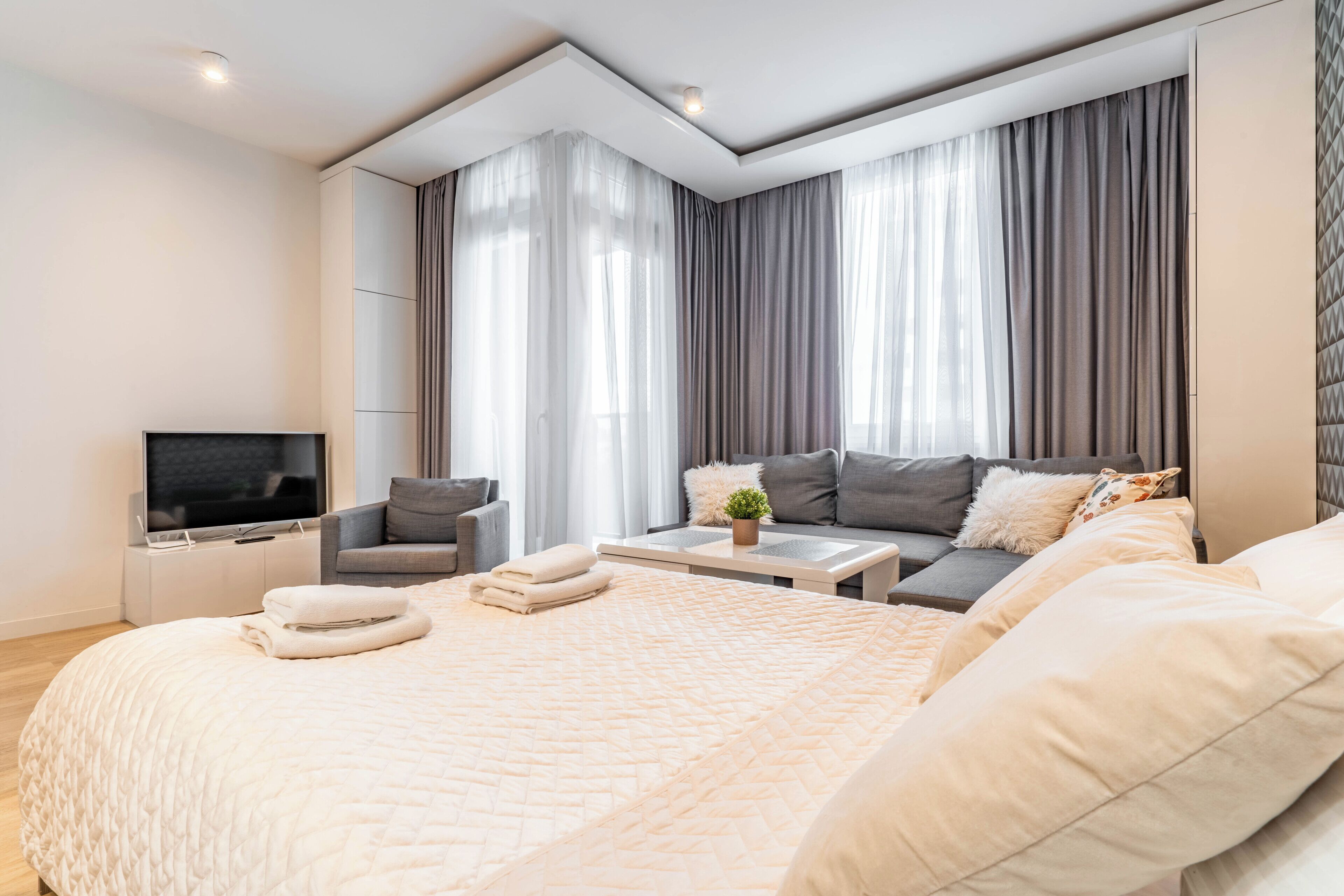 A modern hotel room with a large bed, a sofa, a TV, and a desk.