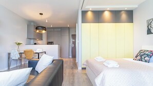 Una habitación de hotel moderna con sofá, cama con cojín floral, zona de comedor y cocina.