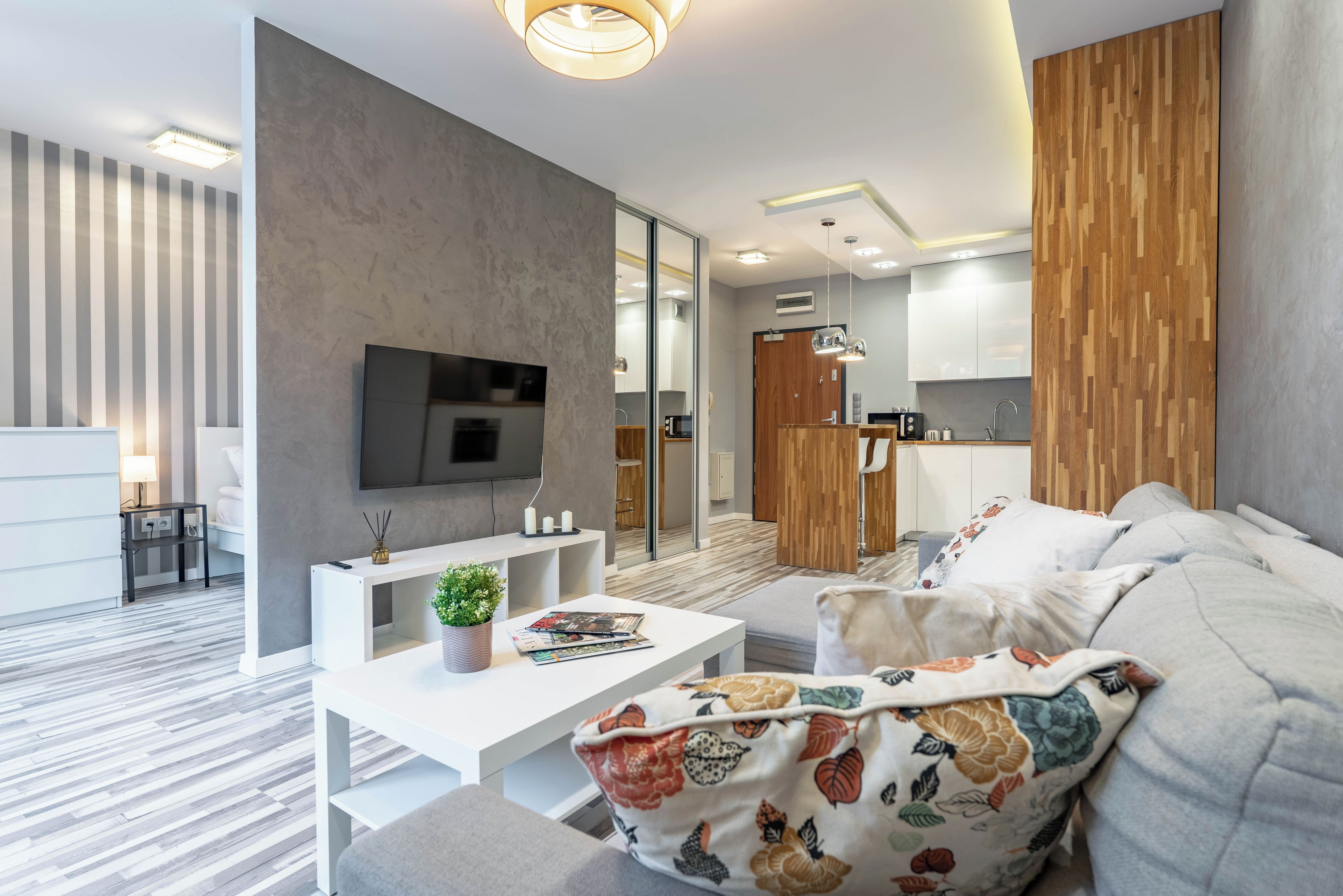 A modern living room with a flat-screen TV, a white console table, and a sofa with floral cushions.